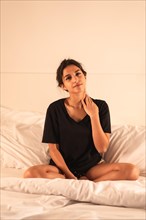 Vertical photo of a young sleepy young woman sitting on the bed