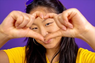 Studio photo with purple background of a cute chinese woman making a heart shape with hands