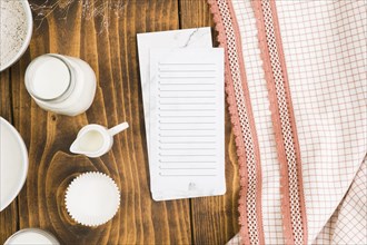 Blank list notepad with milk jar cup cake mold wooden desk near table cloth