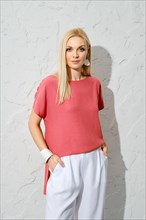 Classy stylish woman with blond hair wearing bright pink shirt and loose white trousers