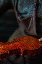 Senior luthier violin maker holding a fresh varnished instrument in his hands in Cremona