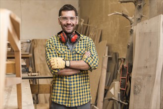 Confident happy carpenter with his arm crossed standing workshop