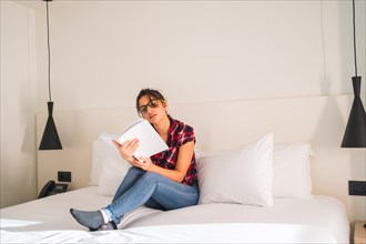 Woman reading a book on the bed of an hotel