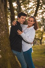 Vertical photo of a young couple embracing leaning on a tree