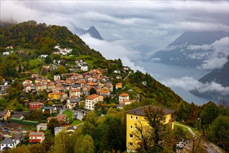 Aerial View over Mountainscape and Alpine Village Bre with Autumn Forest and Lake Lugano in a Cloudy Day in Monte Bre