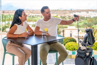Rich man holding a golf club and talking to his couple while drinking cocktails in a terrace
