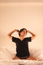 Vertical photo of a woman stretching sitting on the bed in the morning