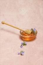 Natural honey in a glass bowl with a wooden spoon and fresh rosemary sprigs in bloom