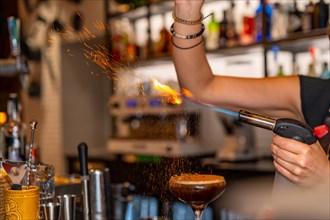 Close-up of the hands of a bartender burning the toppings of coffee cocktail using a torch in a bar