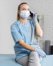 Female physiotherapist with medical mask talking smartphone
