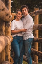 Vertical portrait of a couple looking at camera smiling between wood rails in a park