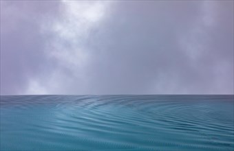 Rippled water surface during rain in swimming pool with dramatic cloudy sky