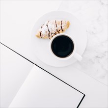 Croissant coffee cup plate near blank page notebook