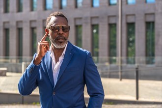 Cool mature african businessman wearing sunglasses and suit using earphones to talking to the mobile outdoors