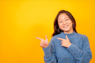 Studio photo with yellow background of a happy chinese woman pointing to the side in a blank space