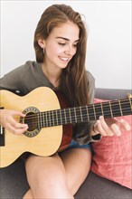 Close up smiling teenage girl playing guitar home