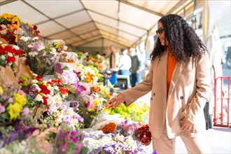 Latin woman wearing warm clothes in autumn walking around a street market with flower shop in the city