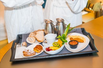 Tray with healthy delicious breakfast served on a hotel room next to a couple in bathrobe