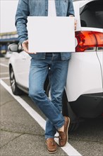 Close up man standing near car road showing blank white placard