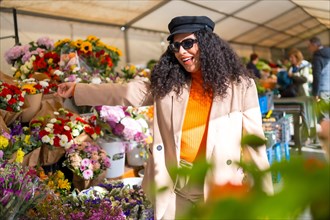 Happy latin woman choosing flowers in an outdoor flower shop in a street market in a sunny day of winter