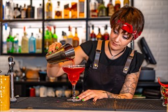 Professional young bartender preparing a red cocktail standing in the counter of a bar