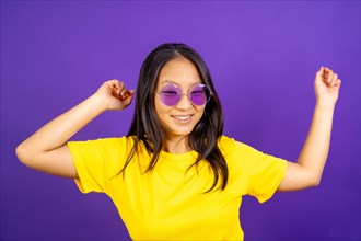 Studio photo with purple background of a chinese woman with sunglasses dancing and smiling