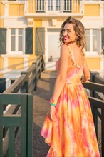 Vertical photo of a beauty woman in long dress turning to smile at camera walking along a beach bridge