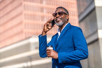 Low angle view portrait of a successful african businessman talking to the phone and drinking coffee outdoors