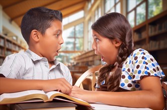 Two hispanic school kids in a library with a shocked expression on their faces