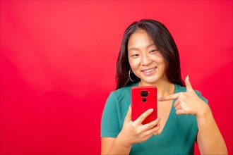 Studio photo with red background of a chinese woman pointing to a mobile phone