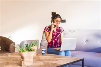 Woman talking to the phone while working from home using laptop