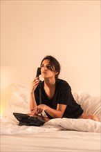 Vertical photo of a woman talking to the phone from the hotel bed