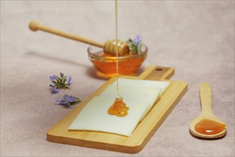 Drizzle of honey dripping on cheese slices with fresh rosemary branches in bloom and a glass bowl with rosemary honey