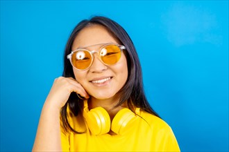 Studio photo with blue background of a shy and cute chinese woman wearing sunglasses smiling at camera