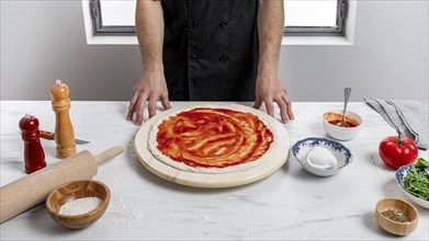High angle man spreading tomato sauce pizza dough