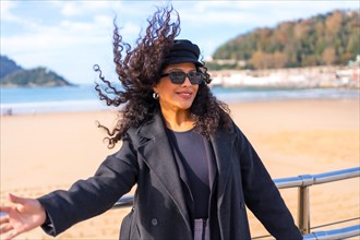 Woman wearing winter clothes and sunglasses move her hair sensually next to a beach