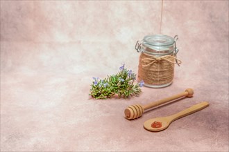 Honey dripping on a wooden spoon with fresh rosemary branches in bloom