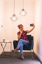Woman waving at camera during a video call with mobile sitting on a cozy room at home