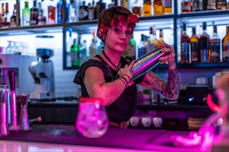 Young female bartender shaking a cocktail with a cocktail shaker in the counter of a bar at night