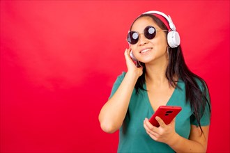 Studio photo with red background of a stylish chinese woman listening to music with mobile phone