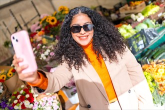 Latin woman taking a selfie next to a flower shop in a market in a sunny day of winter
