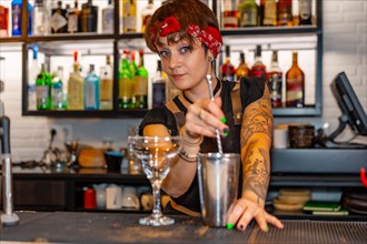 Cute young bartender preparing a cocktail and looking at camera standing in the counter of a bar