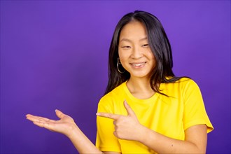 Studio photo with purple background of a positive chinese woman pointing to the side