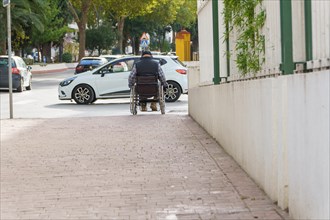 Man in wheelchair seen from the back trying to cross a crosswalk