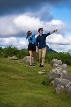 Vertical photo with copy space of a young couple pointing to the landscape standing on a hill in the mountain