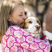 Blond mid adult woman kissing her Beagle dog while he is looking away