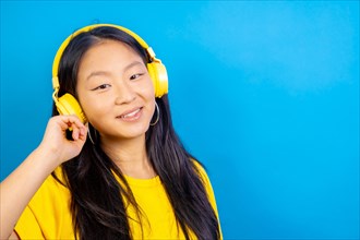 Studio photo with blue background of a chinese woman using headphones smiling at camera