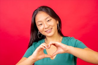 Studio photo with red background of a chinese woman joining hands to symbolize a heart shape