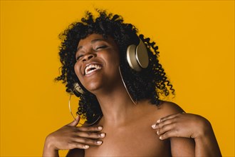 Cheerful naked ethnic young woman earphones studio