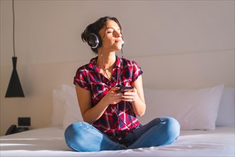 Frontal portrait of a relaxed woman listening to music sitting on a comfortable bed